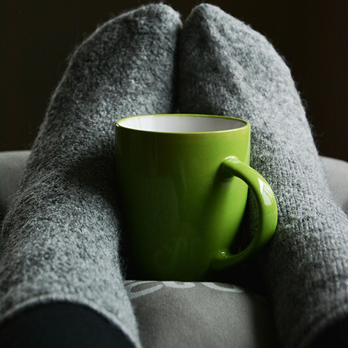 A woman enjoying a warm drink during or after a reflexology session, feet relaxed and supported.